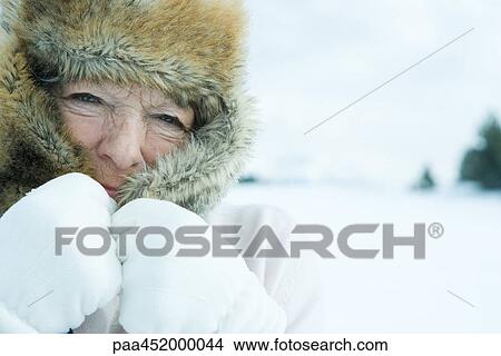Senior woman pulling flaps of fur hat over face, in snowy landscape, close-up View Large Photo Image Picture - Senior woman pulling flaps of fur hat over face, in snowy landscape, close-up. Fotosearch