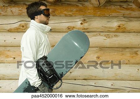 Young man holding snowboard, side view View Large Photo Image Stock Photograph - Young man holding snowboard, side view. Fotosearch