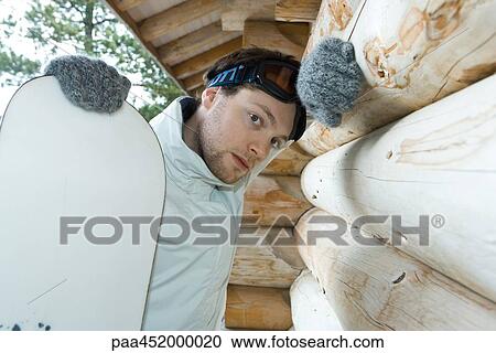 Young man with snowboard, leaning on wall of log cabin, looking at camera View Large Photo Image Stock Image - Young man with snowboard, leaning on wall of log cabin, looking at camera. Fotosearch