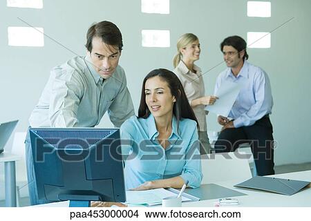 Businessman and businesswoman in office, looking at computer, associates in background View Large Photo Image Picture - Businessman and businesswoman in office, looking at computer, associates in background. Fotosearch