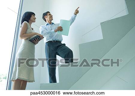 Businessman and young businesswoman standing on stairs, looking up, pointing View Large Photo Image Stock Photograph - Businessman and young businesswoman standing on stairs, looking up, pointing. Fotosearch