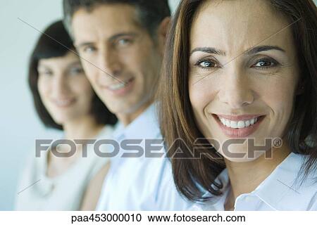 Stock Image - Businesswoman smiling at camera, portrait, business associates in background. Fotosearch