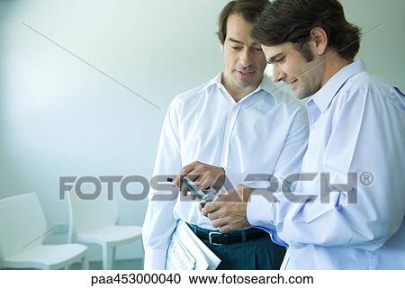 Two businessmen looking at cell phone, pointing, waist up View Large Photo Image Stock Image - Two businessmen looking at cell phone, pointing, waist up. Fotosearch