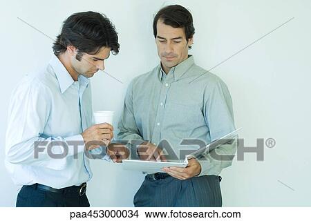 Two businessmen standing, looking at binder, waist up View Large Photo Image Picture - Two businessmen standing, looking at binder, waist up. Fotosearch