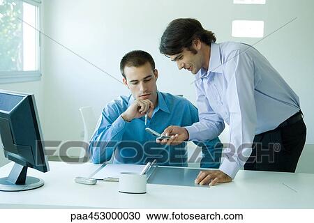 Two young businessmen in office, using cell phone, looking down View Large Photo Image Stock Image - Two young businessmen in office, using cell phone, looking down. Fotosearch