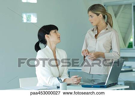 Two young businesswomen in office, looking at each other, discussing View Large Photo Image Stock Photo - Two young businesswomen in office, looking at each other, discussing. Fotosearch