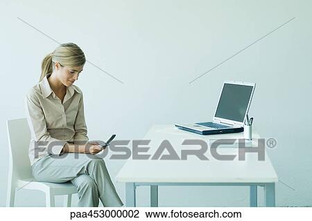 Young businesswoman in office, seated, using cell phone View Large Photo Image Stock Image - Young businesswoman in office, seated, using cell phone. Fotosearch