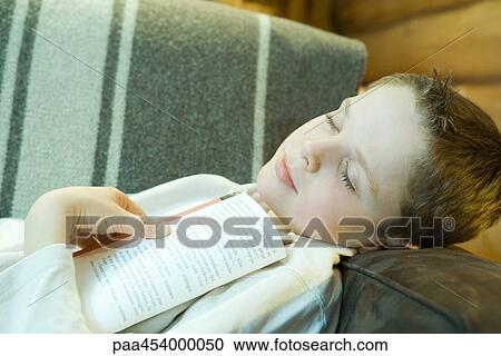 Boy reclining on couch, holding book, eyes closed View Large Photo Image Stock Image - Boy reclining on couch, holding book, eyes closed. Fotosearch