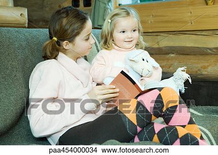 Girl and toddler sitting on couch, reading, smiling View Large Photo Image Picture - Girl and toddler sitting on couch, reading, smiling. Fotosearch
