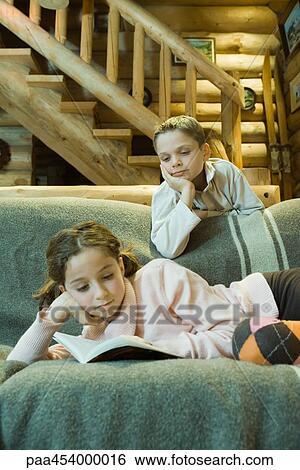 Girl on couch reading book, boy looking over shoulder View Large Photo Image Stock Photograph - Girl on couch reading book, boy looking over shoulder. Fotosearch