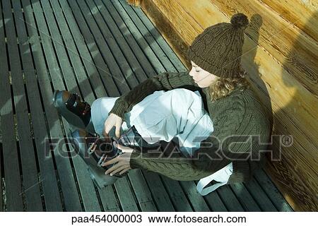Stock Image - Teenage girl sitting on ground, putting on ski boot. Fotosearch