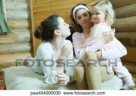 Two teenage girls sitting on bed, one holding toddler on lap View Large Photo Image Stock Image - Two teenage girls sitting on bed, one holding toddler on lap. Fotosearch