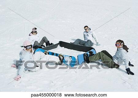 Stock Photo - Four young snowboarders sitting on the ground in a square, looking at camera. Fotosearch