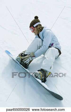 Teenage girl sitting on the ground, putting on snowboard, full length View Large Photo Image Stock Photograph - Teenage girl sitting on the ground, putting on snowboard, full length. Fotosearch