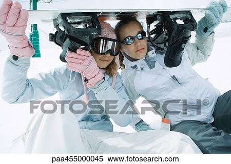 Two teenage girls sitting under snowboard together, smiling at camera View Large Photo Image Stock Photography - Two teenage girls sitting under snowboard together, smiling at camera. Fotosearch