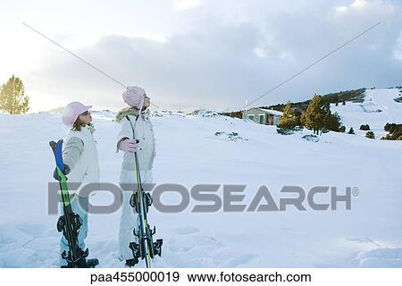 Two young friends standing together, holding skis, looking away View Large Photo Image Stock Photo - Two young friends standing together, holding skis, looking away. Fotosearch