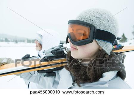 Two young skiers carrying ski on shoulder, looking away, close-up View Large Photo Image Stock Image - Two young skiers carrying ski on shoulder, looking away, close-up. Fotosearch