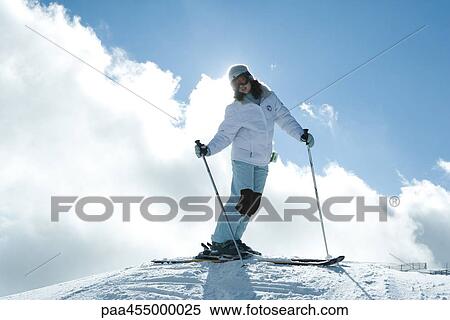 Stock Photography - Young female skier standing on top of ski slope, full length portrait. Fotosearch