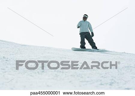 Stock Image - Young man snowboarding on top of ski slope, full length. Fotosearch