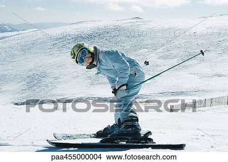 Picture - Young skier bending over, smiling at camera, full length portrait. Fotosearch