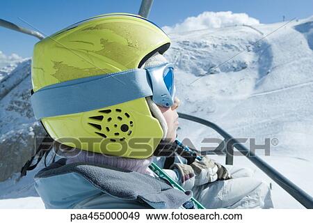 Young skier riding ski lift, wearing helmet, side view View Large Photo Image Stock Photo - Young skier riding ski lift, wearing helmet, side view. Fotosearch