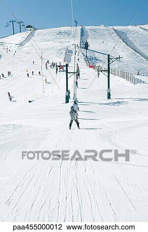 Stock Image - Young skiers using ski lift. in the distance, rear view. Fotosearch