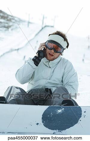 Young snowboarder sitting on the ground, using cell phone, looking at camera View Large Photo Image Stock Photo - Young snowboarder sitting on the ground, using cell phone, looking at camera. Fotosearch