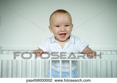 Baby standing in crib, smiling at camera View Large Photo Image Stock Image - Baby standing in crib, smiling at camera. Fotosearch
