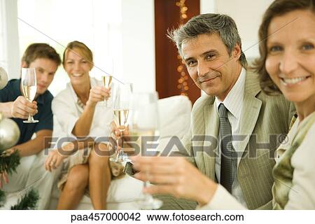 Stock Image - Adult friends making a toast with champagne, smiling at camera. Fotosearch