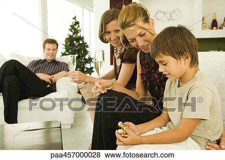 Boy and family sitting on couch, looking at Christmas ornament, Christmas tree in background View Large Photo Image Stock Photo - Boy and family sitting on couch, looking at Christmas ornament, Christmas tree in background. Fotosearch