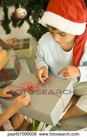 Boy opening Christmas present, wearing Santa hat View Large Photo Image Stock Photo - Boy opening Christmas present, wearing Santa hat. Fotosearch