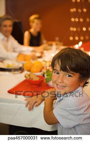 Boy sitting at dinner table, smiling at camera, adults in background View Large Photo Image Stock Image - Boy sitting at dinner table, smiling at camera, adults in background. Fotosearch