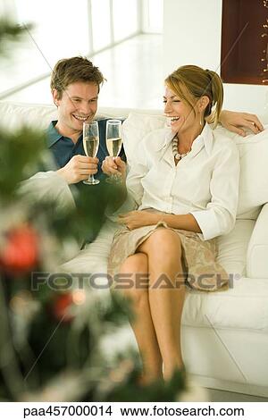 Couple sitting on couch, making a toast with champagne, smiling View Large Photo Image Picture - Couple sitting on couch, making a toast with champagne, smiling. Fotosearch