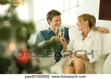 Stock Photography - Couple sitting on couch, making a toast with champagne, smiling at each other. Fotosearch