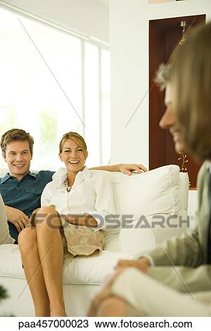 Stock Image - Couple sitting on couch, smiling, friends in foreground. Fotosearch