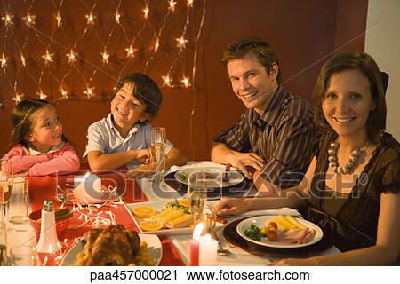 Stock Image - Family with two children eating festive dinner, smiling at camera. Fotosearch