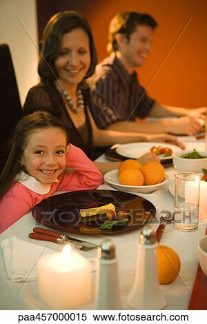 Girl sitting at dinner table, smiling at camera, adults in background View Large Photo Image Stock Photography - Girl sitting at dinner table, smiling at camera, adults in background. Fotosearch