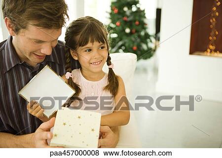 Stock Photo - Girl sitting on man's lap, opening Christmas present, smiling. Fotosearch