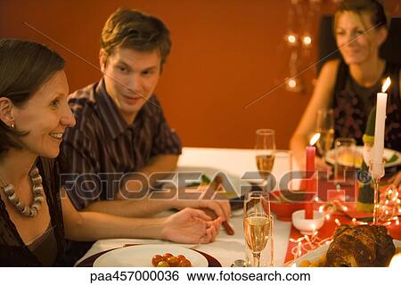 Stock Photograph - Three adult friends eating Christmas dinner, looking at each other, smiling. Fotosearch