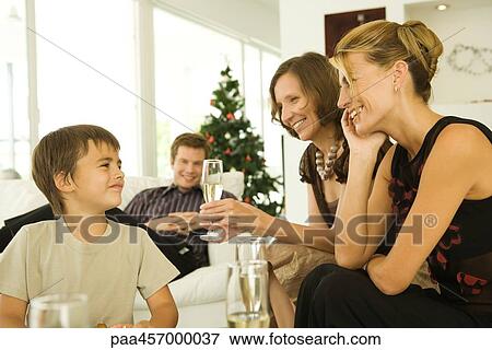 Stock Photo - Three adults drinking champagne, smiling at boy, Christmas tree in background. Fotosearch
