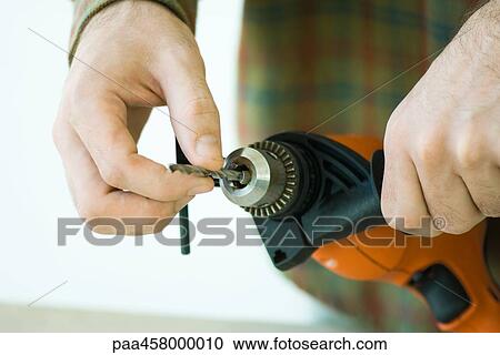 Stock Image - Man adjusting drill bit, cropped view of hands. Fotosearch