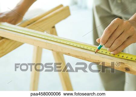 Stock Photograph - Unrecognizable person measuring wood with measuring tape. Fotosearch