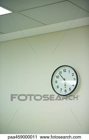 Stock Image - Clock hanging on wall under fluorescent light. Fotosearch
