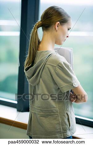 Stock Image - Female student looking out window, side view. Fotosearch