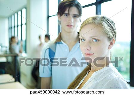 Stock Image - Female student smiling at camera, sideways glance, male peer in background. Fotosearch