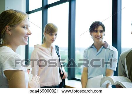 Stock Image - Group of students standing by window, smiling, waist up. Fotosearch