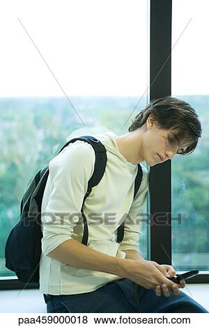 Male student in front of window, looking at cell phone View Large Photo Image Stock Photo - Male student in front of window, looking at cell phone. Fotosearch