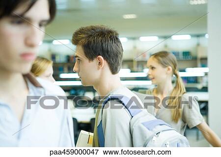 Stock Photo - Students walking in library, side view. Fotosearch