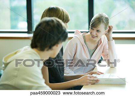 Stock Image - Three students sitting at table, chatting. Fotosearch