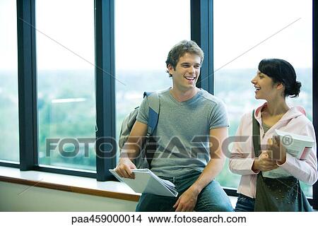Two students chatting in front of window, smiling at each other View Large Photo Image Picture - Two students chatting in front of window, smiling at each other. Fotosearch